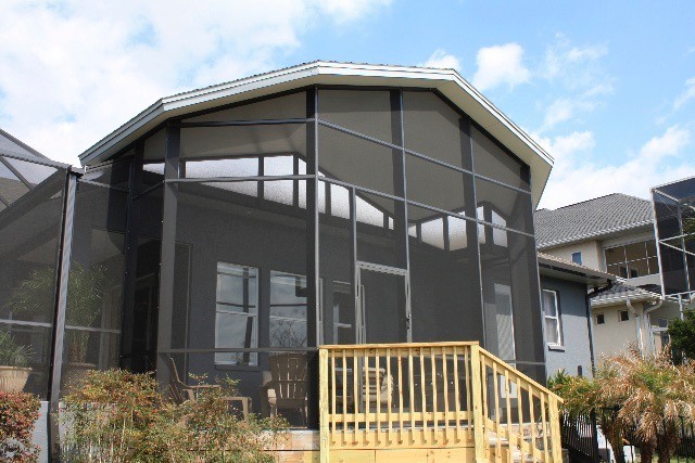 A tall screen room in a backyard with chairs and a table inside.