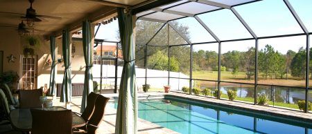 A screened in pool and patio area complete with furniture and a large blue pool.