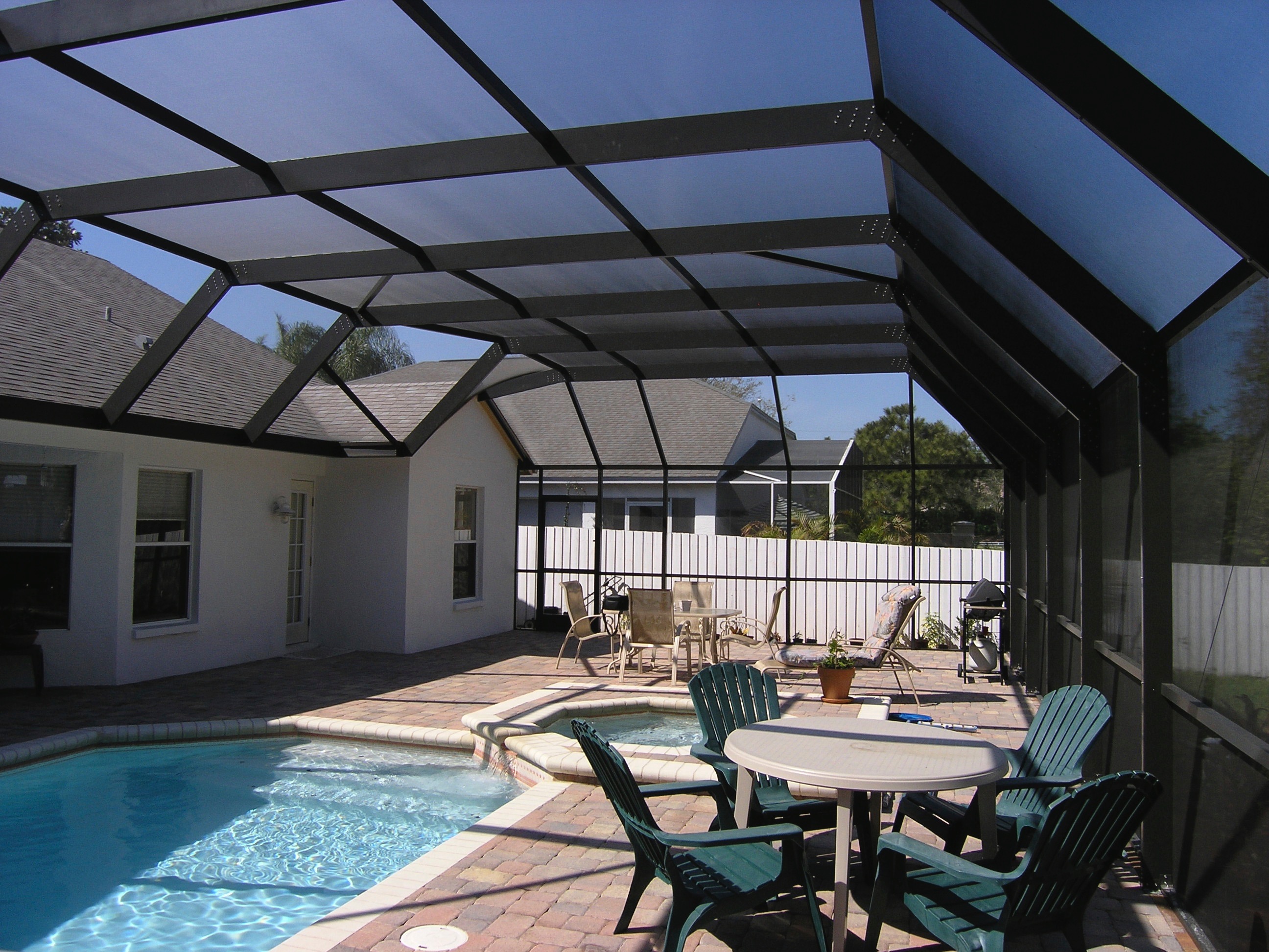 A beautiful screened in backyard space complete with a pool, chairs, and tables.