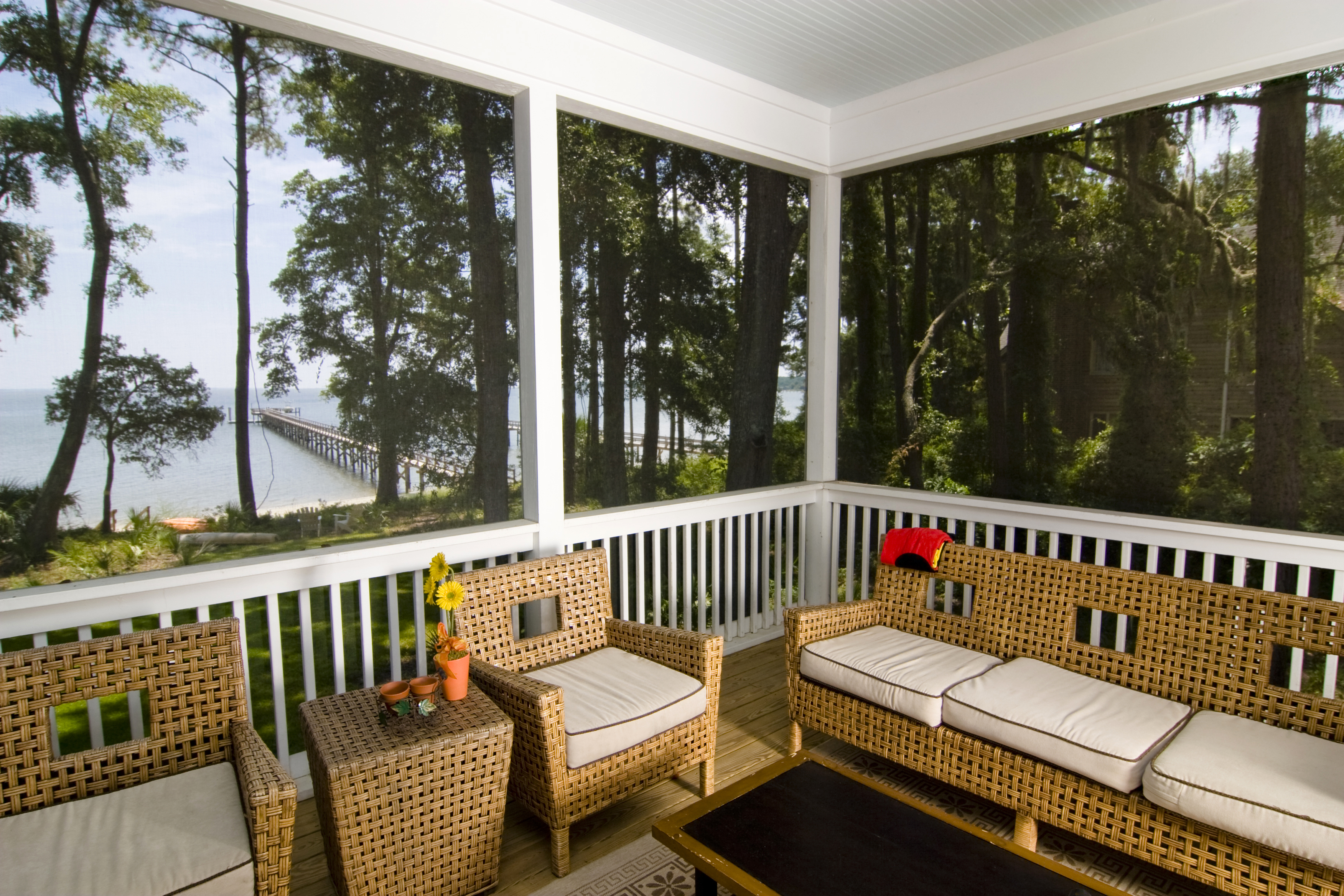 A screened-in porch with chairs and tables and a view of a lake in the background.